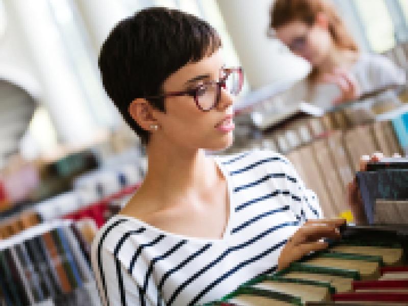 A woman in a striped shirt looking at books.